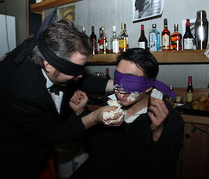 Two blindfolded expeditioners feed each other cake at a murder mystery party