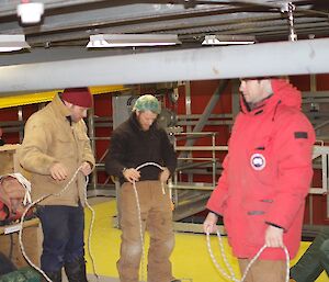 Three men standing up holding lengths of rope in their hands.