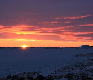 The sun descends beyond the horizon, barely glimpsed as it turns the sky a brilliant orange and purple