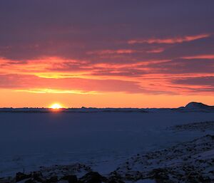 The sun descends beyond the horizon, barely glimpsed as it turns the sky a brilliant orange and purple