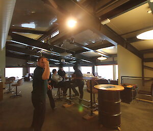 Man in bar playing darts, three onlookers in conversation behind