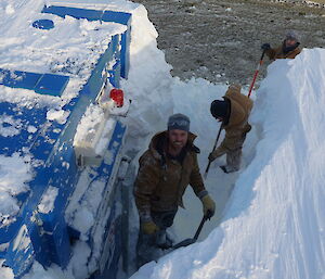 Three men digging a trench to the entrance of a building