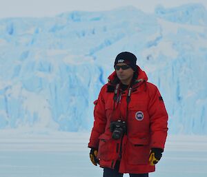 Man standing with camera around his neck, glacier behind him in distance