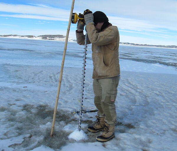 Adam Christensen drilling the sea ice