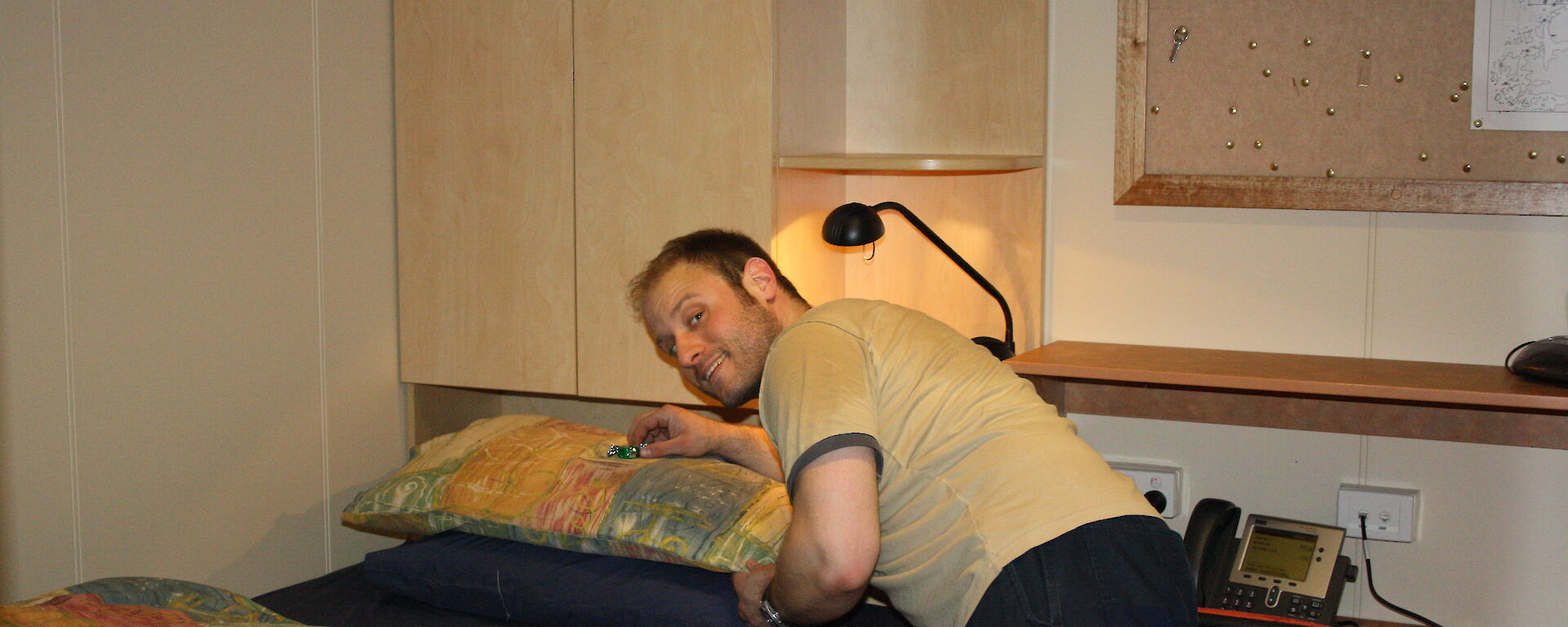 Man leaving a chocolate on the pillow of a single bed.