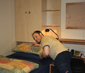 Man leaving a chocolate on the pillow of a single bed.