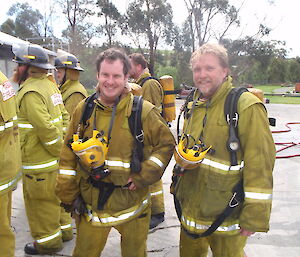 Two tired expeditioners pose smiling in full fire fighting gear
