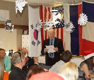 Graeme standing in front of foreign flags while he says grace before the commencement of dinner.