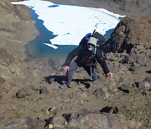 An expeditioner climbing up a steep hill with a lake as a backdrop