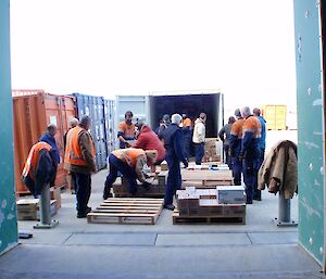 A large group of people unloading a container of food into the station store.