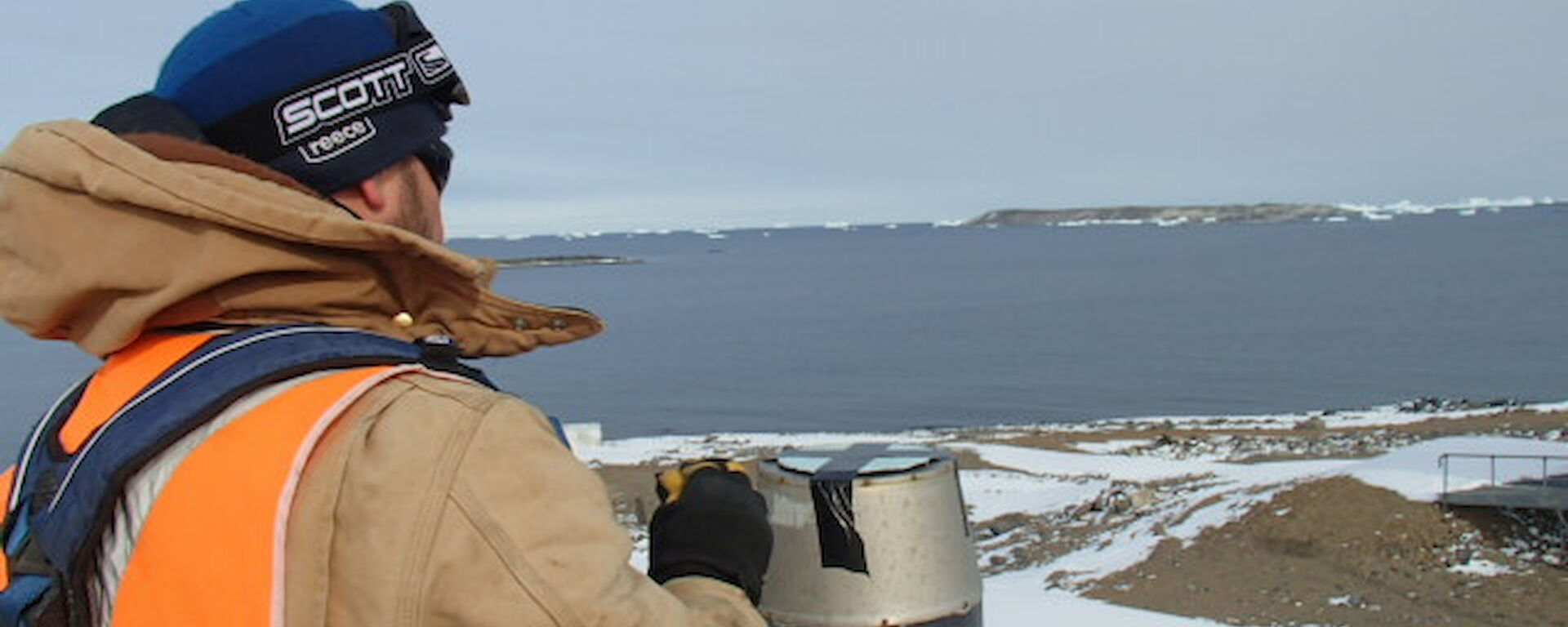 Paul taping a cover on an exhaust vent with ice bergs in the distance.