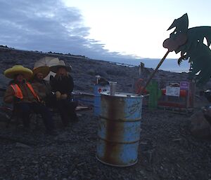 Three expeditioners wearing Mexican hats sitting at the refuelling point with fake palm trees and cactus plants
