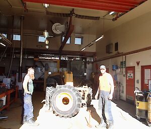 Two diesel mechanics wearing singlets after changing a large JCB tyre in the work shop with the main workshop door open