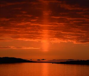 A bright orange beam of sun light going straight up into the sky directly above the sun as it sets