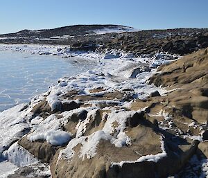 Frozen sea spry turning the shoreline rocks white with pancake ice formations on the water