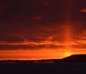 A bright orange beam of sun light going straight up into the sky directly above the sun as it sets