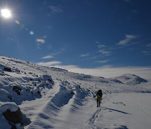 An expeditioner walks on the edge of the bay through the snow on a beautiful clear day