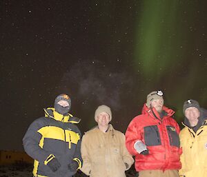 Four expeditioners dressed in their cold weather gear out enjoying the aurora in the night sky
