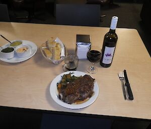 A steak dinner with garlic bread, dips and a glass of red wine served on the table
