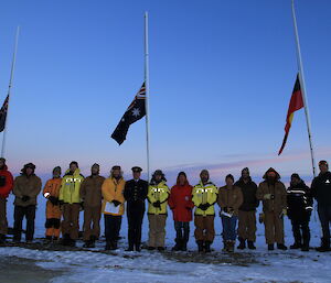 The wintering crew at Davis stand before the Australian, Aboriginal and New Zealand flags flying at half mast