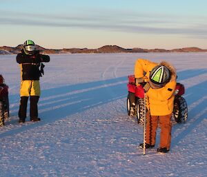 Expeditioner drilling a hole in the sea ice with a battery drill on a long sea ice drill bit