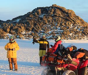 Three expeditioners standing around a quad bike out on the sea ice