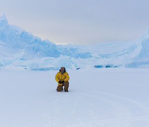 Gavin kneels in front of an iceberg moored in the sea ice