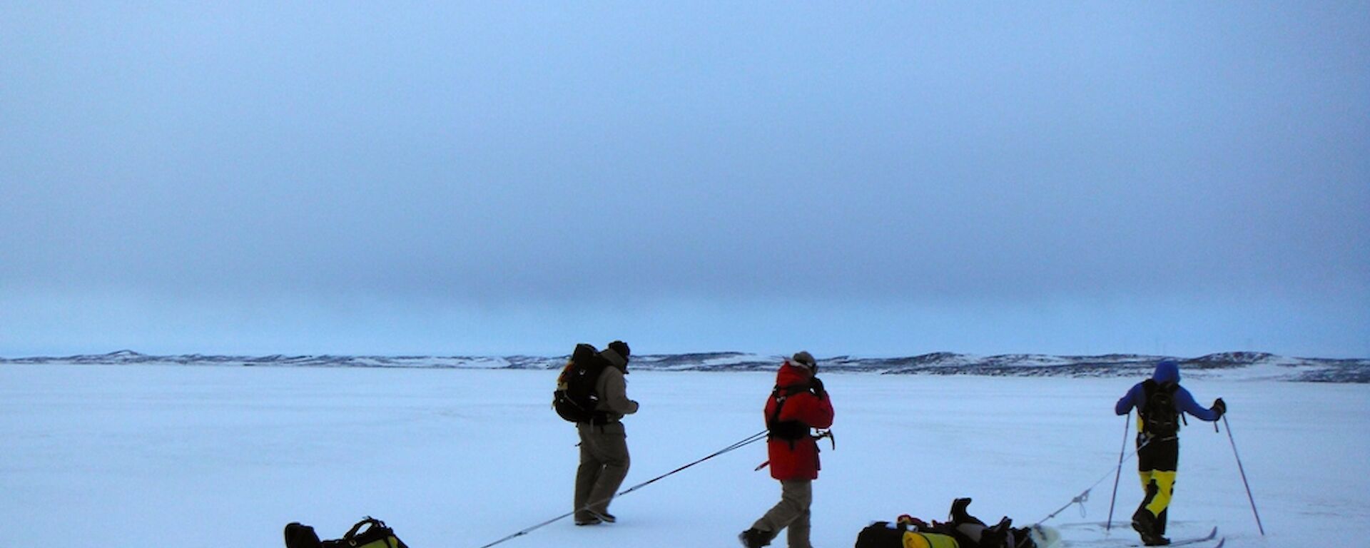 Two expeditioners walking and one cross country skiing dragging a sled on the sea ice