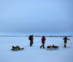 Two expeditioners walking and one cross country skiing dragging a sled on the sea ice