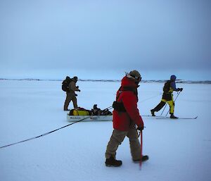 An expeditioner dragging a sled while walking on the sea ice with two expeditioners in the background