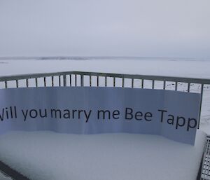 The “Will you marry me” sign standing up in the snow on the outside table