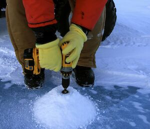 Expeditioner drill the ice with a battery drill to gauge the thickness