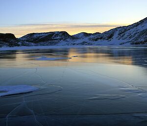 Photo of the smooth top of a frozen fresh water lake with hills in the background