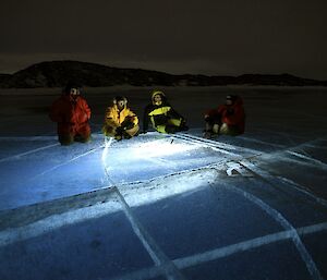 Four expeditioners on the frozen fresh water lake with the ice lit up by a torch