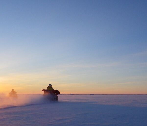 Expeditioners on three quads riding on the sea ice into the rising sun