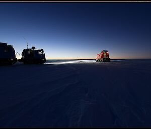 Red and blue over snow vehicle parked on the ice with headlights on