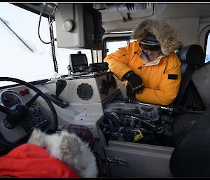 Two expeditioners clearing snow and ice out of the engine bay from the inside of the Hägglunds