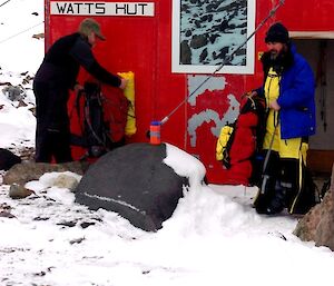 Tow expeditioners in front of Watts Hut with their hiking packs