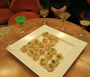 A plate of canapés surrounded by cocktails in martini glasses