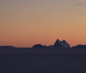 An iceberg that looks like Cradle Mountain stands on the horizon in the midday twilight