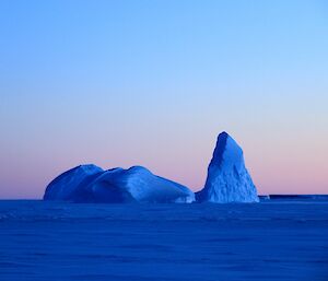 The twilight makes the icebergs look bright blue with a pink sky behind