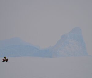 Expeditioner on quad stops to look at large iceberg