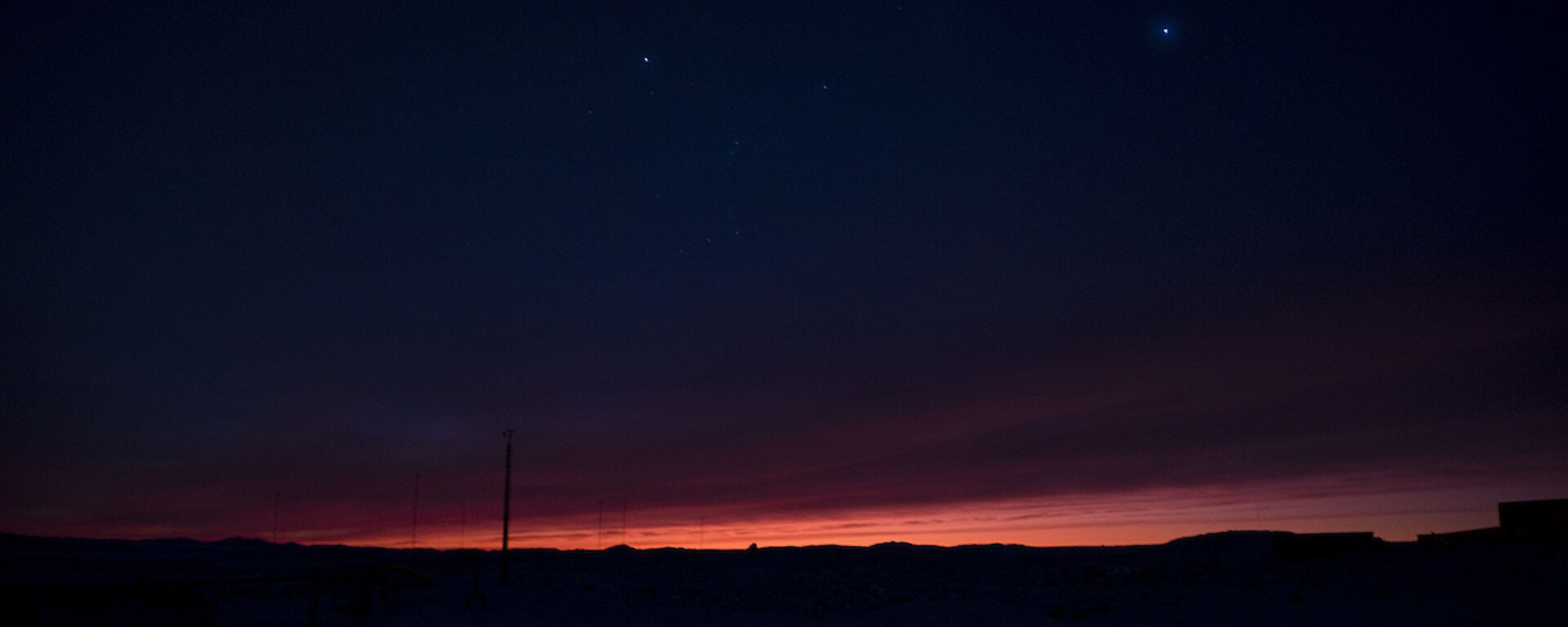 Orange dawn breaks on the horizon with star field above
