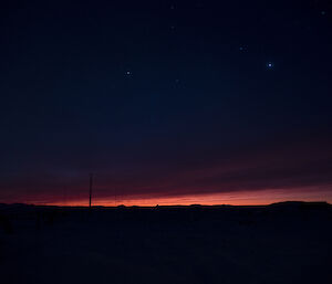 Orange dawn breaks on the horizon with star field above