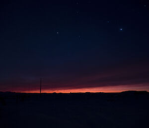 Orange dawn breaks on the horizon with star field above