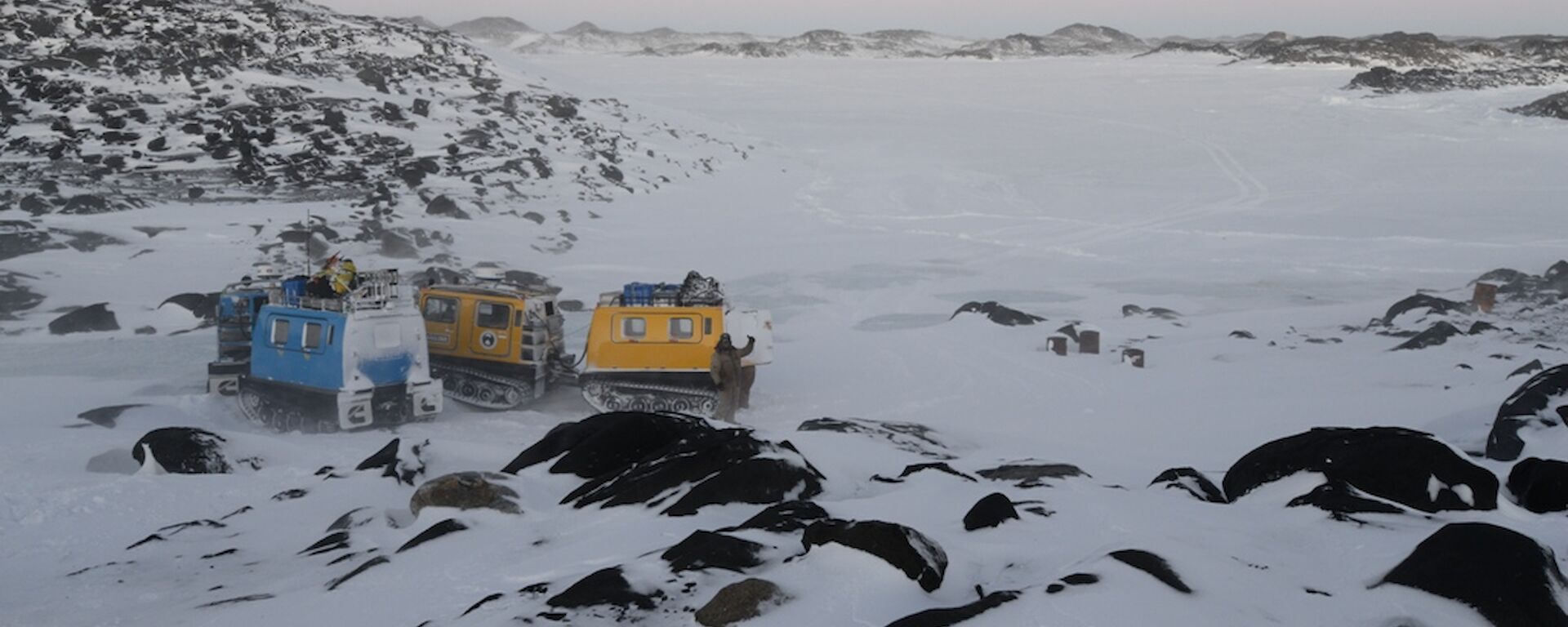 The blue and yellow Hägglunds parked close to each other with the frozen fjord in the background