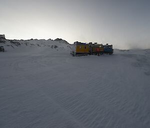 The yellow and blue Hägglunds parked up with Bandits hut to the left of picture and blowing snow to the right