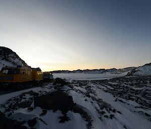 The yellow and blue Hägglunds parked on the land bridge with the end of the frozen sea ice of Tryne Fjord in the background