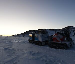 The blue Hagg loaded up with equipment and towing a trailer with the portable power supply unit strapped to it while traversing on the frozen sea ice in Tryne Fjord