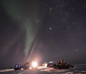 The night sky at Whoop Whoop filled with bright stars and an awesome Aurora drifting across the huts and with the over snow vehicles in the foreground